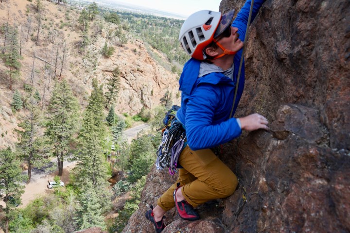 Person rock climbing in a blue jacket and helmet on a tall cliff.