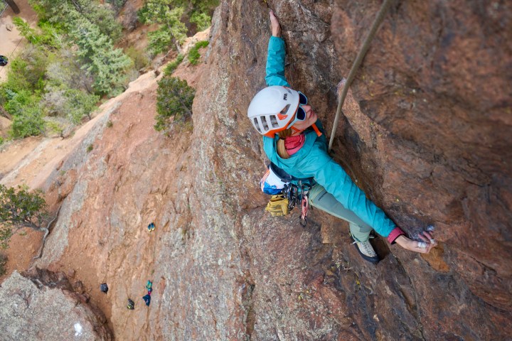 Person rock climbing a steep cliff face with safety gear and helmet.