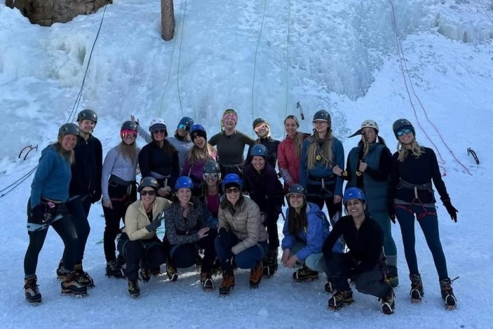 Group of people in climbing gear posing in front of an icy cliff.