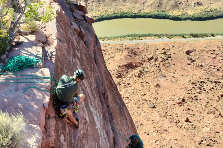 Two rock climbers on a cliff overlooking a river and canyon.