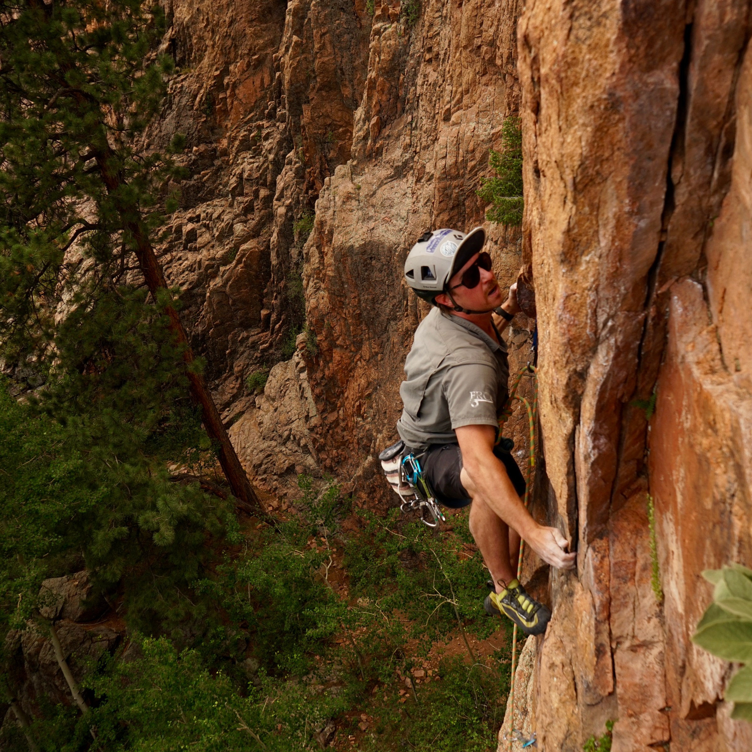 Rock climber ascending a steep cliff face with safety gear and helmet.