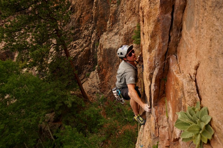 Rock climber ascending a steep cliff face with safety gear and helmet.