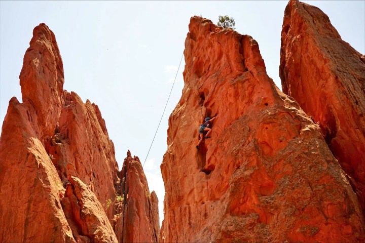 Person rock climbing on tall, red sandstone formations.