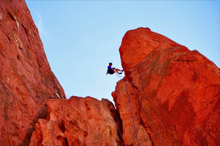 Person rock climbing on red sandstone under clear blue sky.