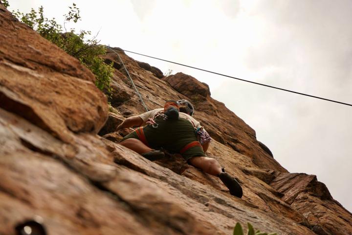 Person rock climbing on a steep brown cliff face.